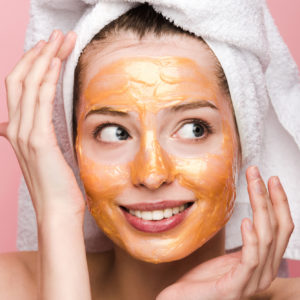 Girl in an orange face mask with a towel on her head and her hands around her face, revealing collarbone